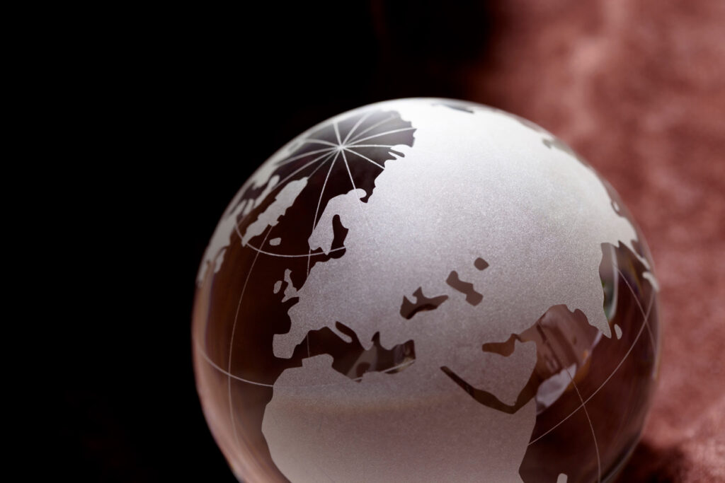 Imagem de uma esfera de vidro que apresenta um mapa-múndi com destaque para a Europa, Ásia e África, refletindo uma superfície espelhada e lisa.